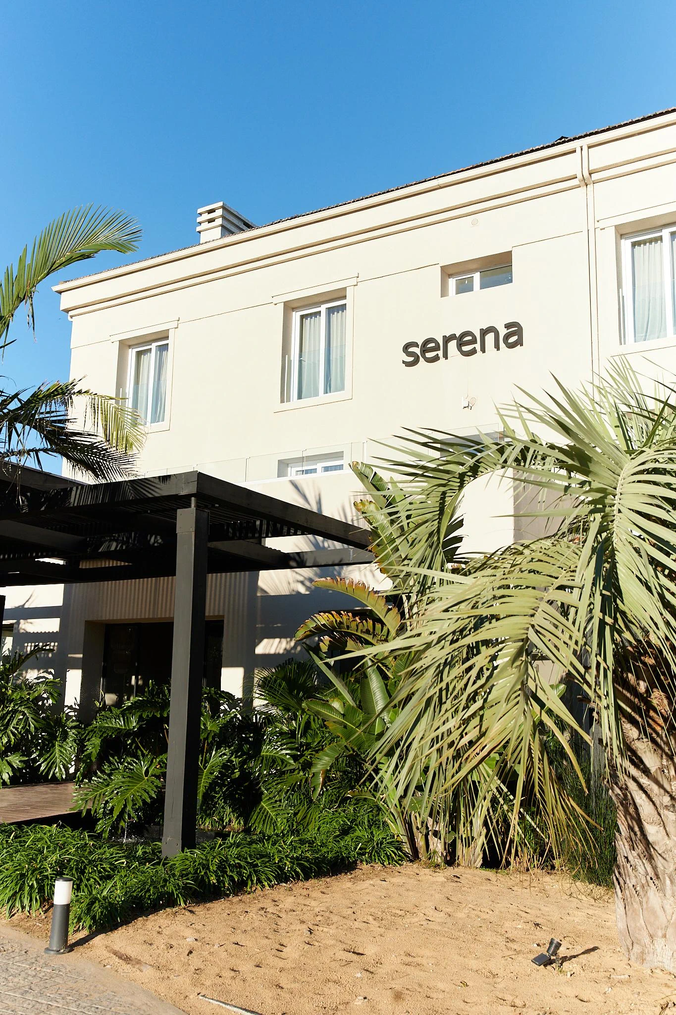 Facade of Serena Hotel with palm trees and clear blue sky.